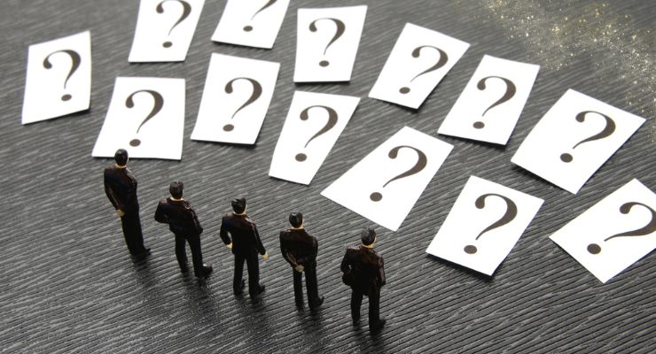 選択肢を前に立つビジネスマンの模型とクエスチョンマークのカード｜意思決定や課題解決を表すビジネスイメージ