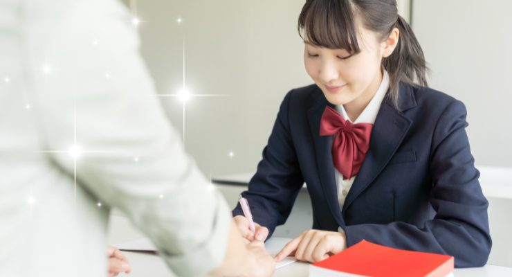 高校生が書類に署名する場面｜進路相談や入学手続きの様子を示すイメージ