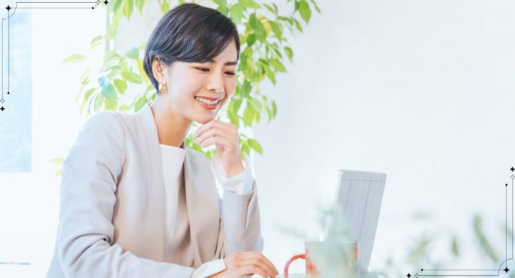 ノートパソコンを見ながら微笑む女性のオフィスワーク風景｜オンライン会議や在宅勤務を行うビジネスシーンのイメージ