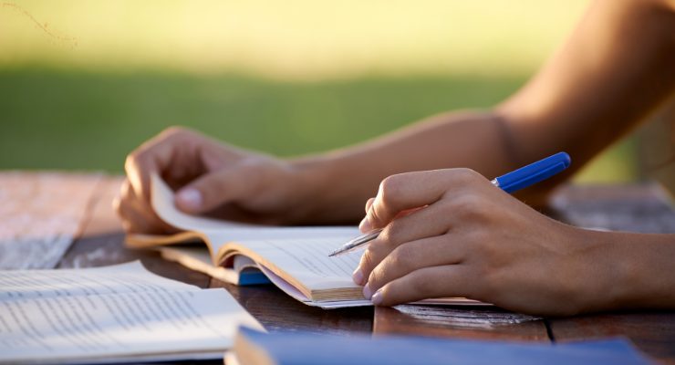 ノートにペンで書き込みをする手元のアップ写真｜屋外で勉強する学習風景イメージ