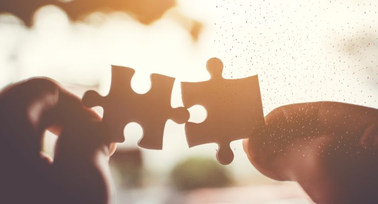 夕陽の中でパズルのピースを合わせようとしている手|つながりや協力、問題解決のイメージ